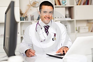 Smiling physician filling up medical forms on laptop