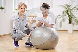 Smiling physiotherapist with elderly woman laying on exercising ball during physical therapy photo
