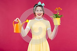 Smiling pinup girl holding flowers in pot and watering can