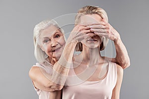 Smiling pleasant senior woman covering eyes of her beautiful daughter