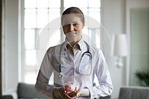 Smiling pleasant young female doctor holding piggybank in hands.