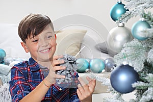 Smiling portrait child decorate the christmas tree with pine cone and balls at home