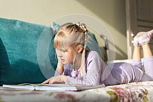 Smiling portrait little cute adorable happy blond caucasian kid girl enjoy lying on sofa bed and reading fairy tale