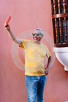 Smiling portrait of older man leaning against wall looking at cell phone