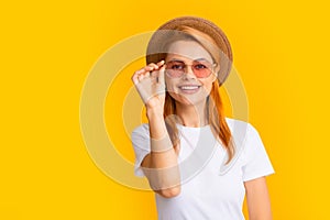 Smiling portrait of pretty young woman wearing sunglasses and straw hat over yellow background. Happy girl enjoying
