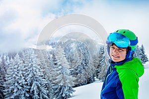 Boy in ski helmet and mask smile standing over forest