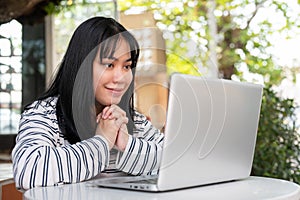 A smiling and positive Asian woman is working remotely outdoors in a city park, using her laptop