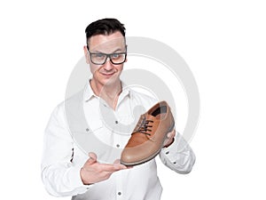 Smiling positive businessman in a white shirt and glasses holds a shoe in his hands showing the buyer, isolated on white