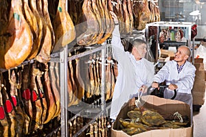 Smiling positive butchery technologists checking joints of iberico jamon