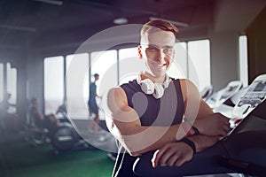 Smiling positive confident male personal instructor with arms crossed arms near treadmill at gym in fitness gym