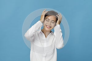 Smiling positive female with attractive look, wearing white T-shirt, posing against blue blank wall