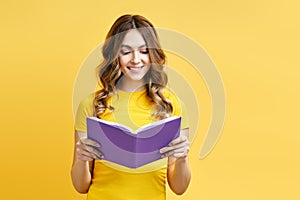 Smiling positive girl reading book on yellow background