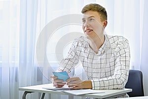 Smiling positive male student answering teacher in high school classroom