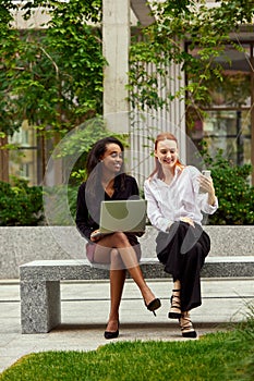 Smiling, positive office workers, stylish women sitting outside office, working and having online video call