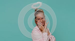 Smiling positive shy angelic teenager girl with angel halo nimb over head, celebrating holidays