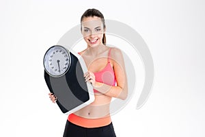 Smiling positive young fitness woman in sportwear holding weighing scale