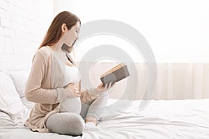Smiling pregnancy reading ibook sitting on bed