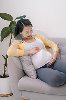 Smiling pregnant asian woman sitting on the sofa