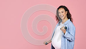 Smiling pregnant brunette lady exercising with barbells on pink background