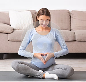 Smiling pregnant girl making heart on her belly