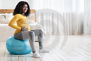 Smiling pregnant lady exercising on fitness ball