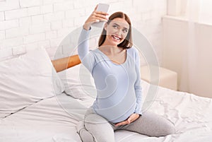 Smiling Pregnant Lady Taking Selfie On Smartphone Sitting On Bed