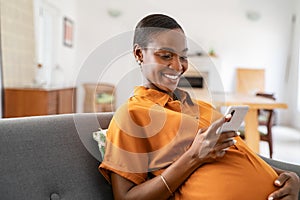 Smiling pregnant mid adult black woman messaging on mobile phone