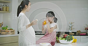 Smiling pregnant mother and daughter enjoys being in the kitchen together