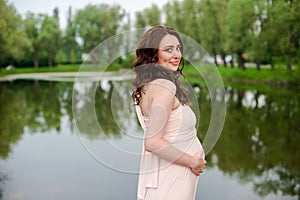 Smiling pregnant woman 25-29 year old resting by the lake. Posing outdoors. Motherhood. Maternity.