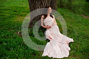 Smiling pregnant woman 25-29 year old resting by the lake. Posing outdoors. Motherhood. Maternity.