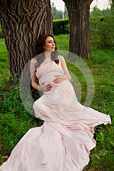 Smiling pregnant woman 25-29 year old resting by the lake. Posing outdoors. Motherhood. Maternity.