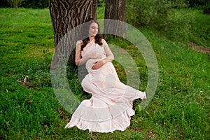 Smiling pregnant woman 25-29 year old resting by the lake. Posing outdoors. Motherhood. Maternity.