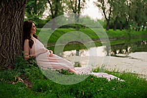 Smiling pregnant woman 25-29 year old resting by the lake. Posing outdoors. Motherhood. Maternity.