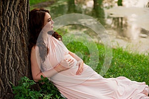 Smiling pregnant woman 25-29 year old resting by the lake. Posing outdoors. Motherhood. Maternity.