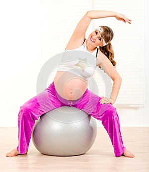 Smiling pregnant woman doing exercises on ball