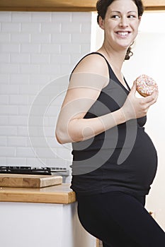 Smiling Pregnant Woman With Doughnut In Kitchen