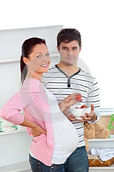 Smiling pregnant woman eating strawberries at home