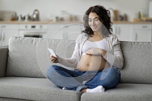 Smiling pregnant woman embracing belly and looking at her baby sonography image