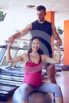 Smiling pregnant woman exercising in gym with personal trainer