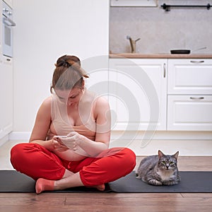 Smiling pregnant woman learns fitness in home kitchen by phone online