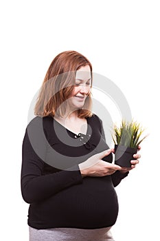 Smiling pregnant woman looking at a pot of grass