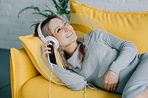 smiling pregnant woman lying on sofa and listening to music