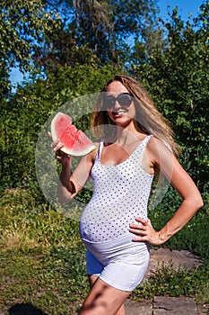 Smiling pregnant woman and a piece of red watermelon in summer