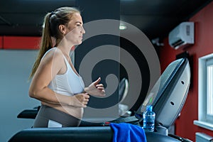 Smiling pregnant woman running on a treadmill. The concept of a healthy lifestyle, sport during pregnancy
