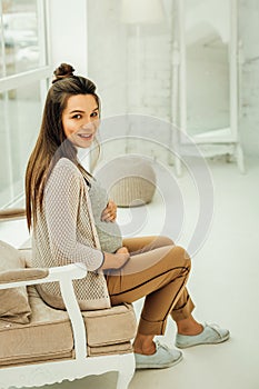 Smiling pregnant woman sitting in the armchair