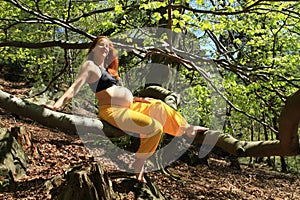 Smiling pregnant woman sitting on branch