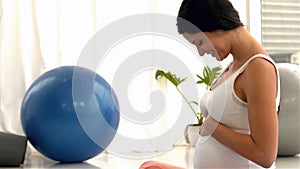 Smiling pregnant woman sitting on mat touching her belly