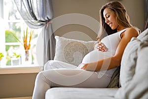 Smiling pregnant woman sitting in sofa looking at her stomach