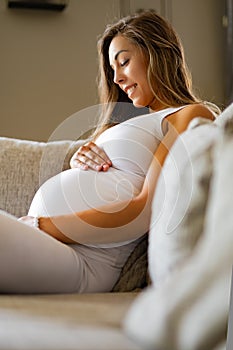 Smiling pregnant woman sitting in sofa looking at her stomach