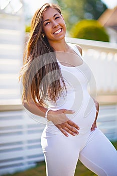 Smiling pregnant woman standing in garden holding on tummy